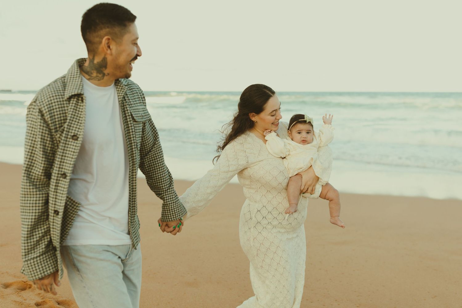 Three people enjoying a breezy day at the beach while walking along the sandy shore together.
