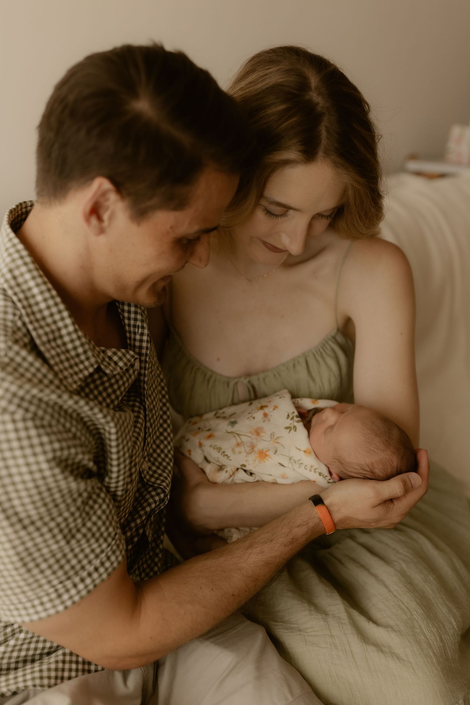Intimate family moment with parents gazing at their newborn in warm sepia tones.