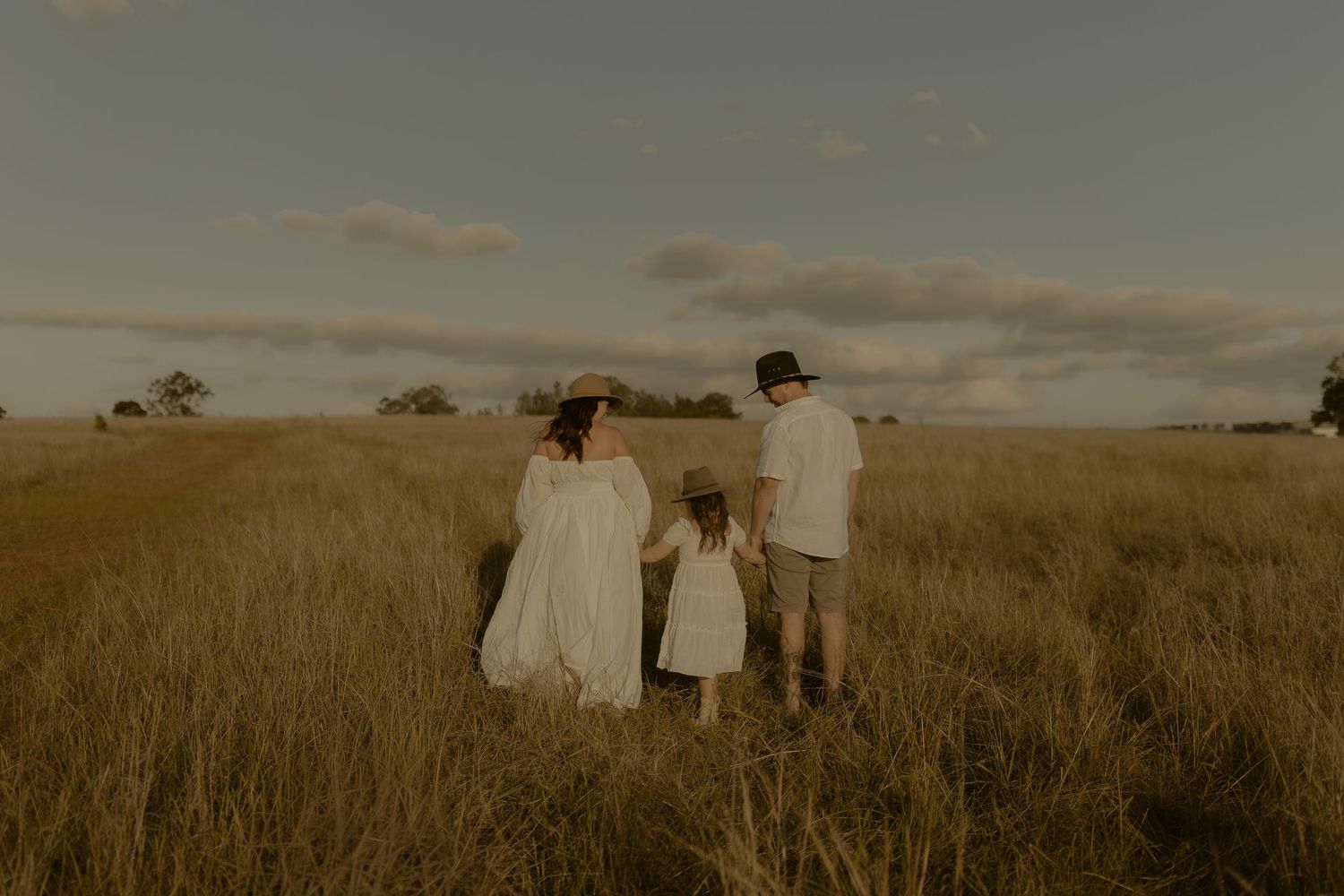 A group of people walking through a golden field at sunset with warm lighting and tall grass.
