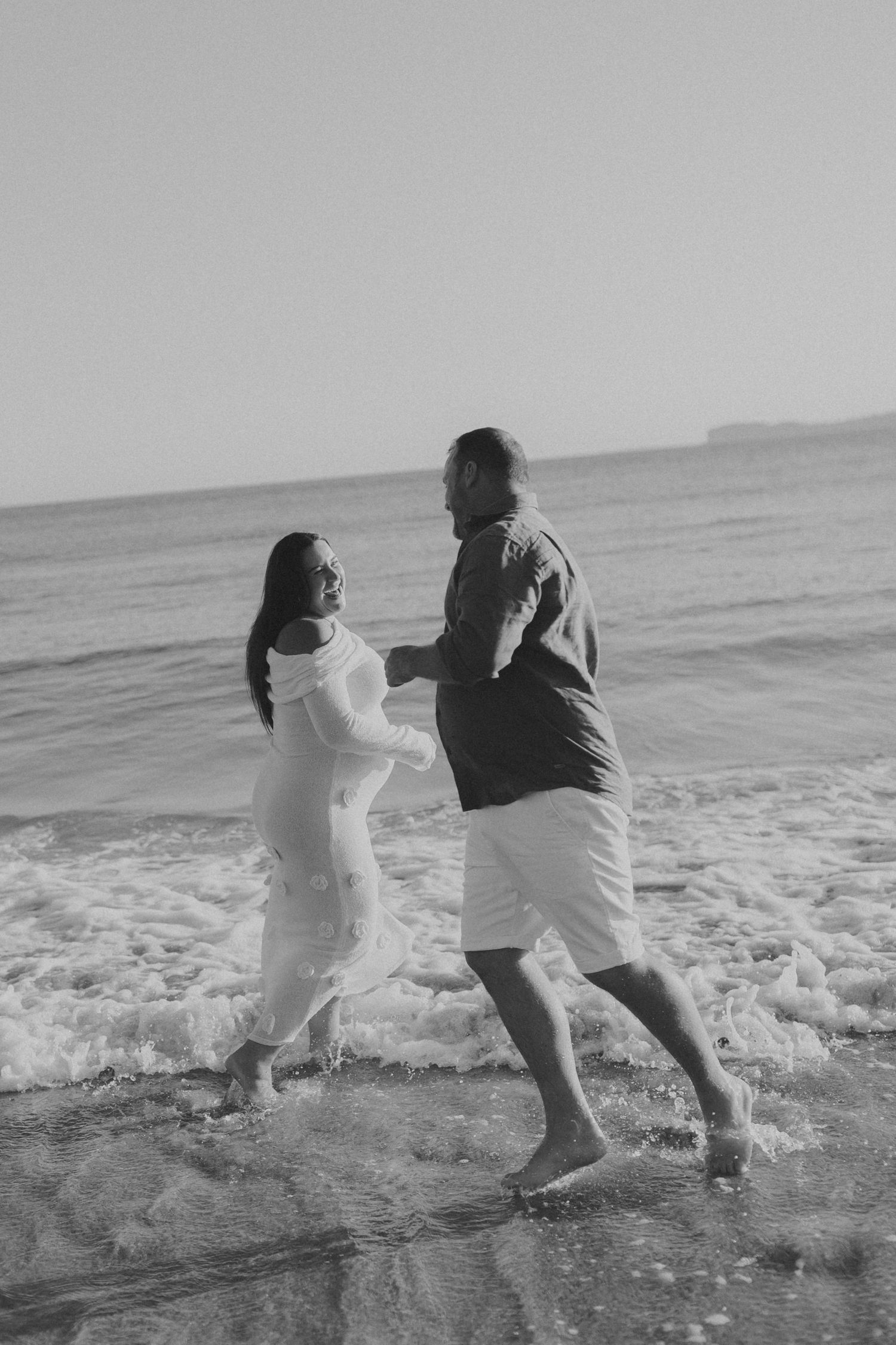 Black and white photo of a couple splashing and playing in the ocean waves at the beach.