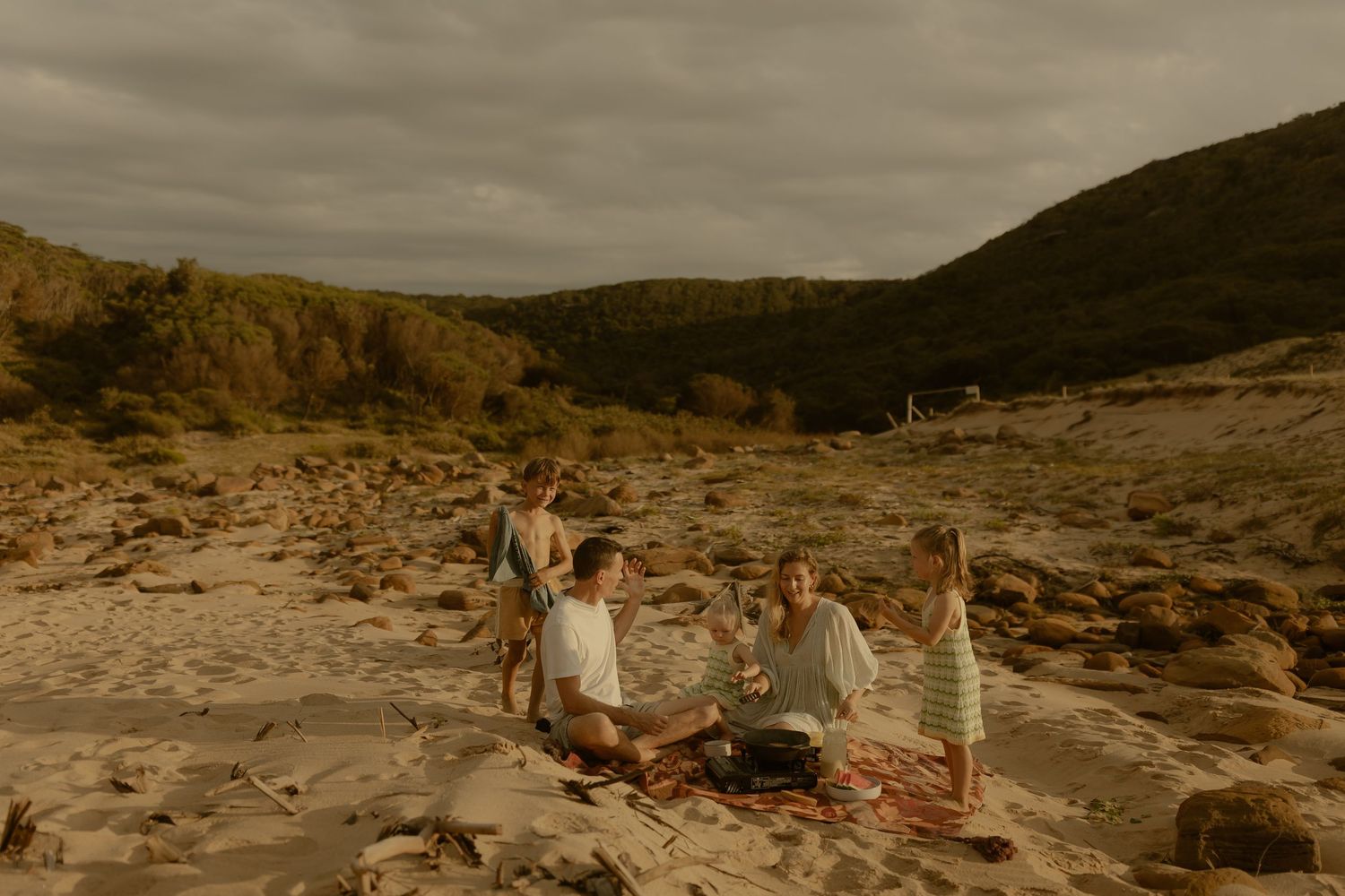 A scenic picnic gathering on rocky coastal terrain under cloudy skies at sunset.