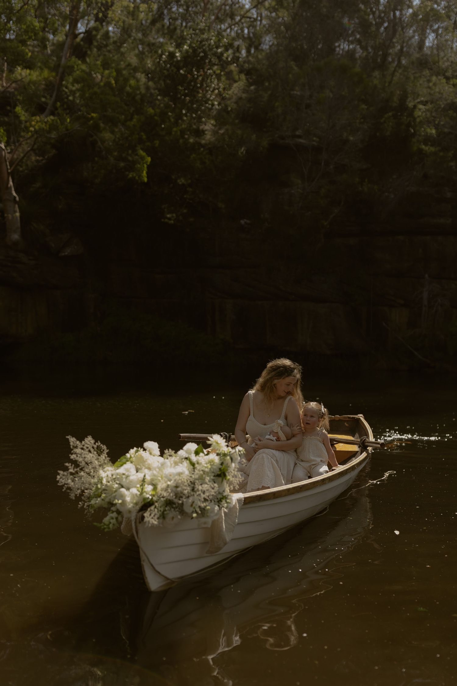 A romantic scene of a white canoe adorned with flowers floating on dark water in a wooded setting.