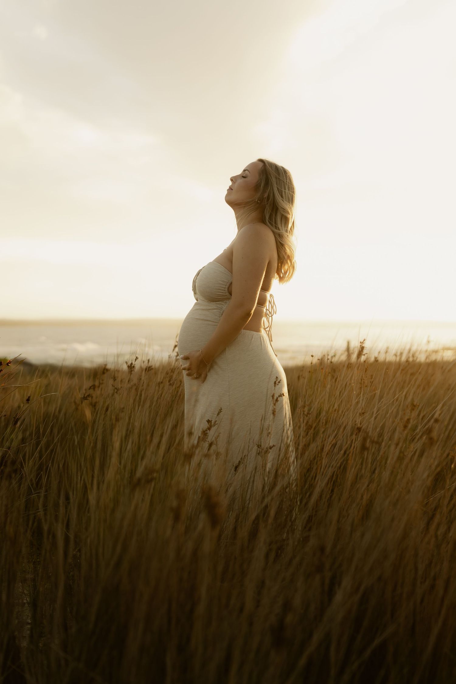 Silhouette of person in white dress standing among tall grass during sunset.