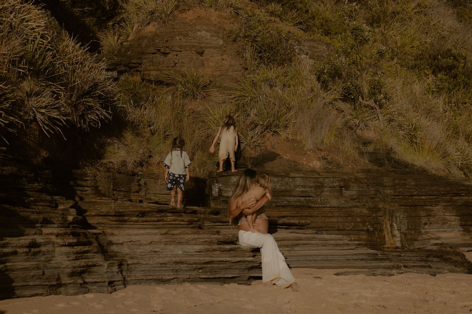 People walking up stone steps on a rocky hillside in warm golden sunlight.