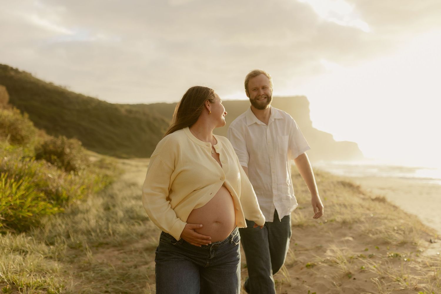 Couple embraces during golden hour photoshoot on scenic coastal cliffs at sunset.