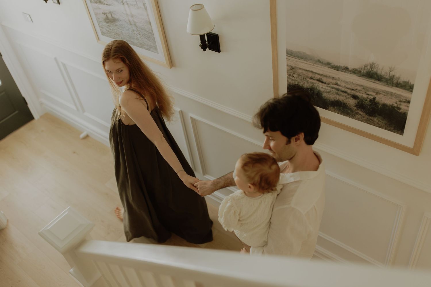 A young family with a baby walks down a bright staircase, sharing a tender moment in their cozy home.