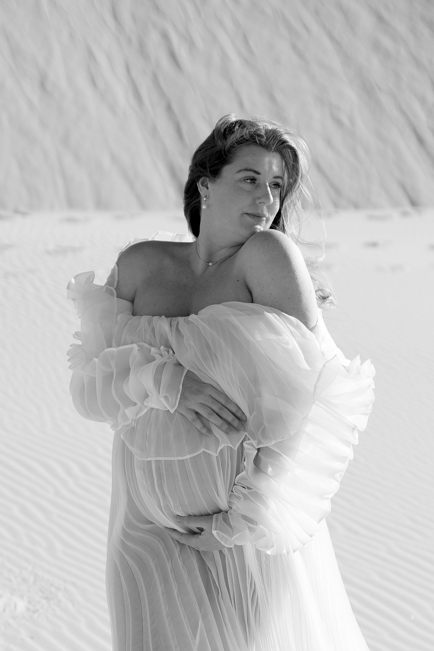 A black and white artistic portrait of a woman in flowing white fabric against sand dunes.