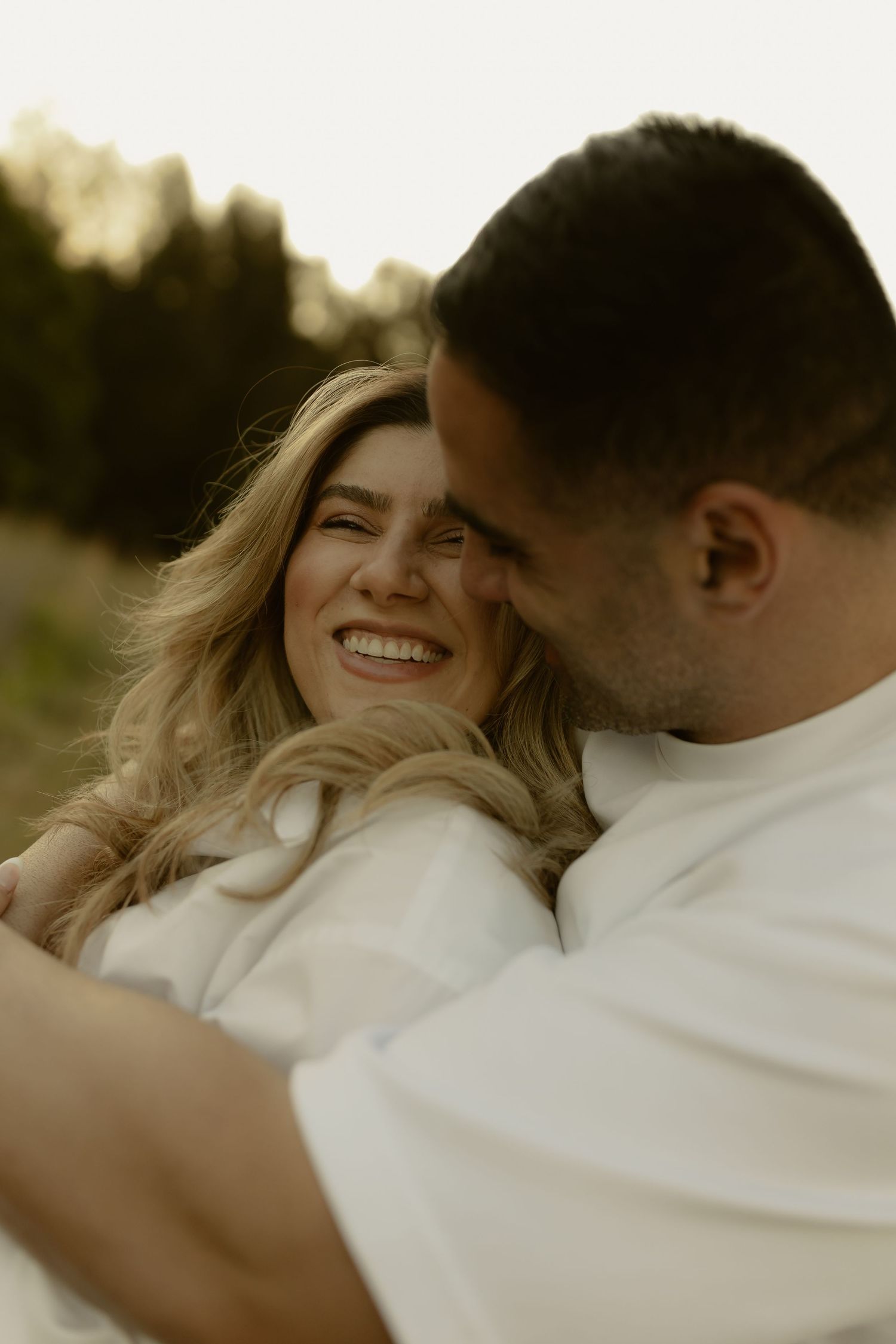 Happy couple embracing and laughing together outdoors in warm golden sunset light.