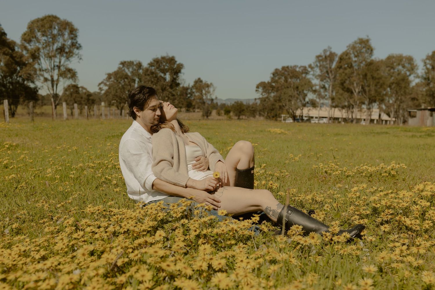 Two people relax together in a sunny meadow filled with yellow wildflowers on a warm afternoon.