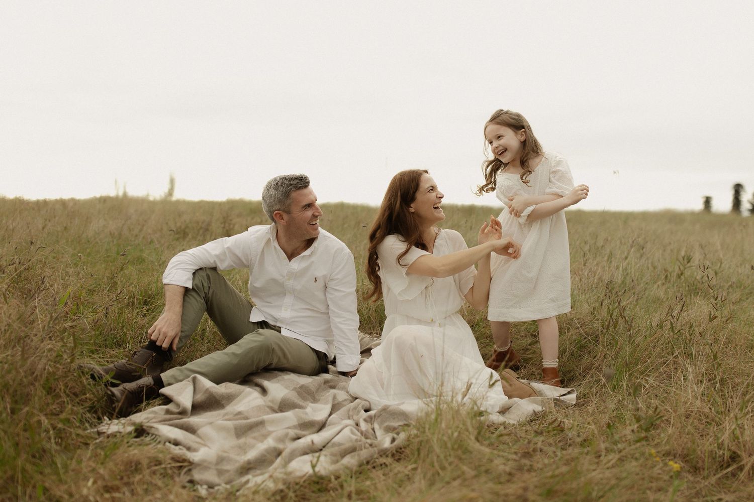 A family relaxes together on a blanket in a scenic grassy field during sunset.