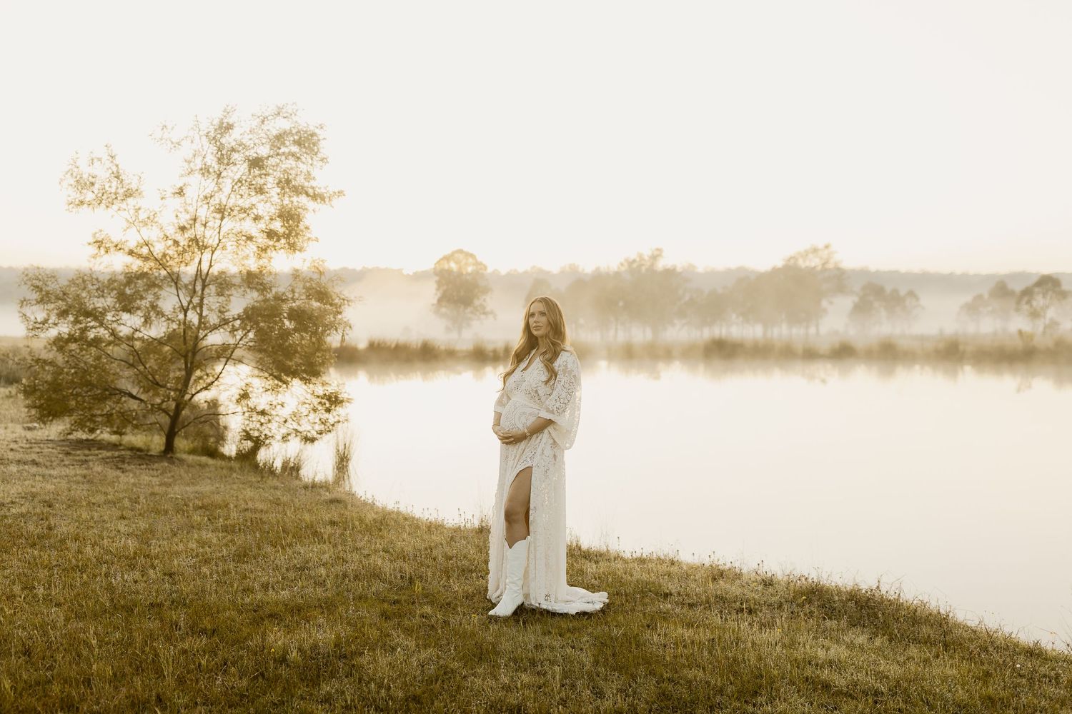 A dreamy sepia-toned scene shows a figure in white dress sitting by a misty lake at sunset.