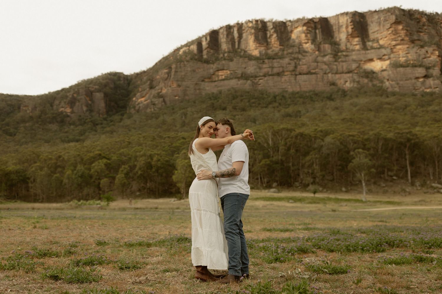 A romantic embrace in front of dramatic cliff faces during golden hour.