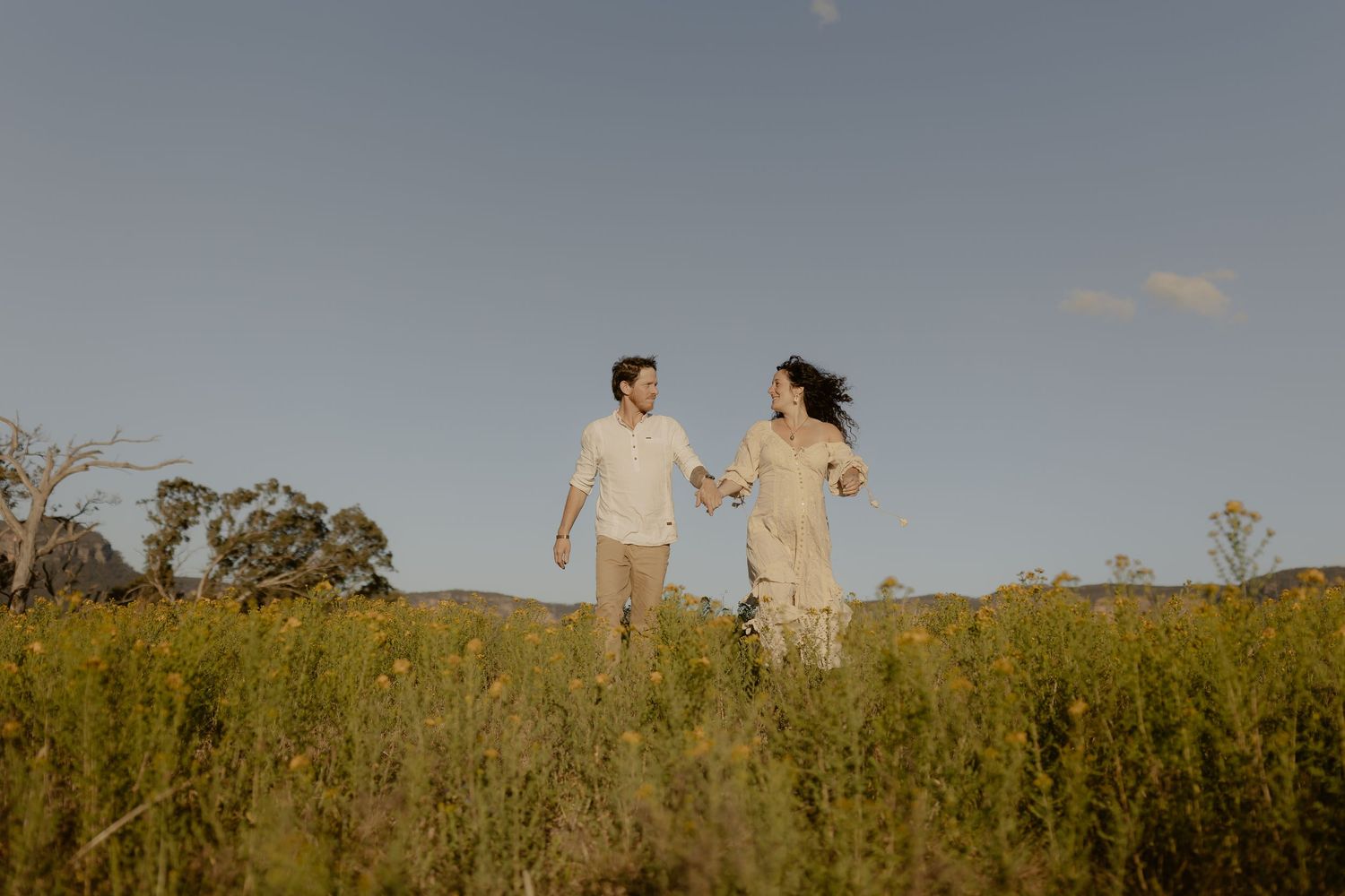 A couple stands together in a sunlit meadow during golden hour.