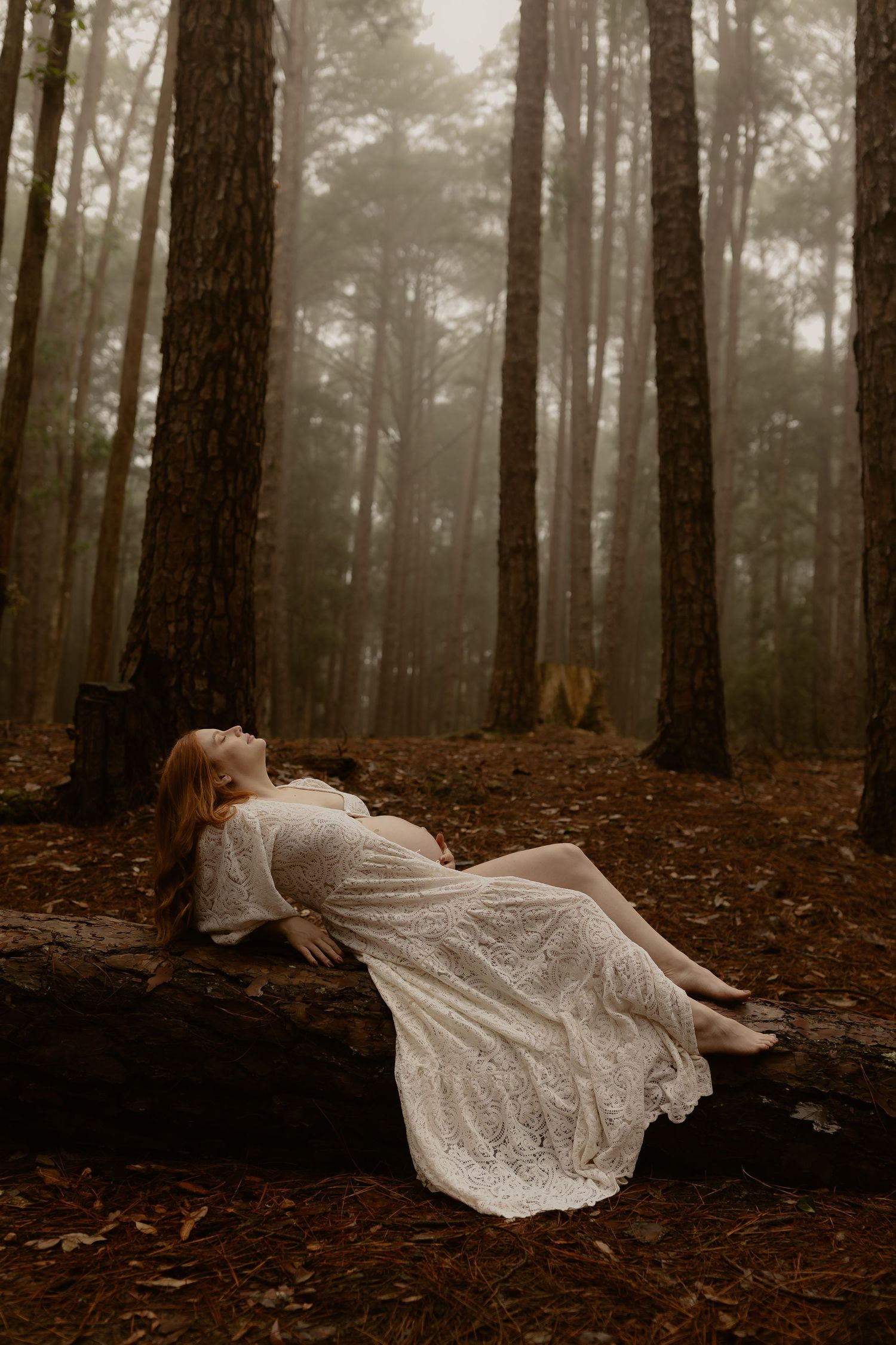 A figure in a white lace dress lies ethereally on a misty forest floor covered in fallen leaves.
