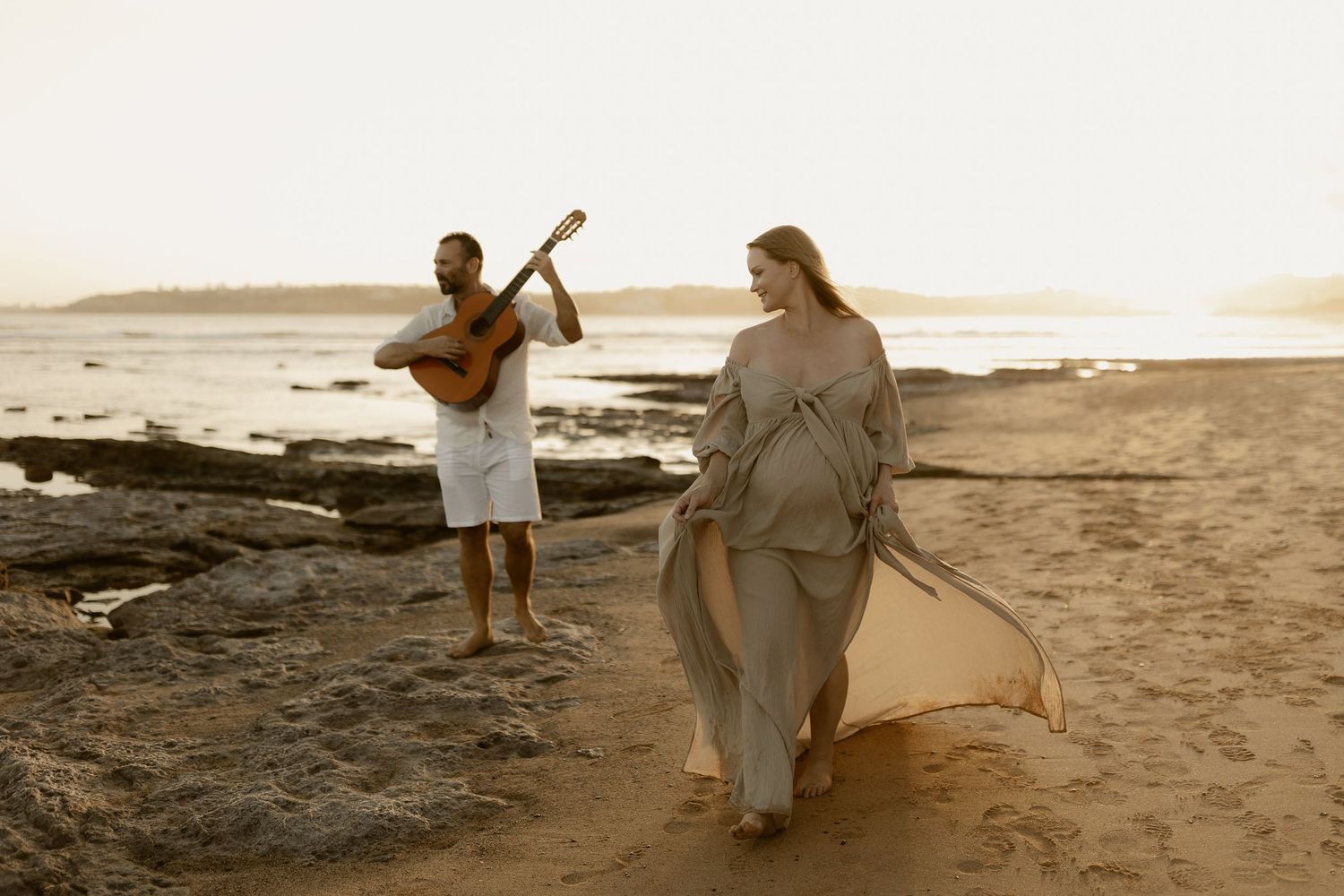People in light colored clothing strolling on a sandy beach during golden hour.