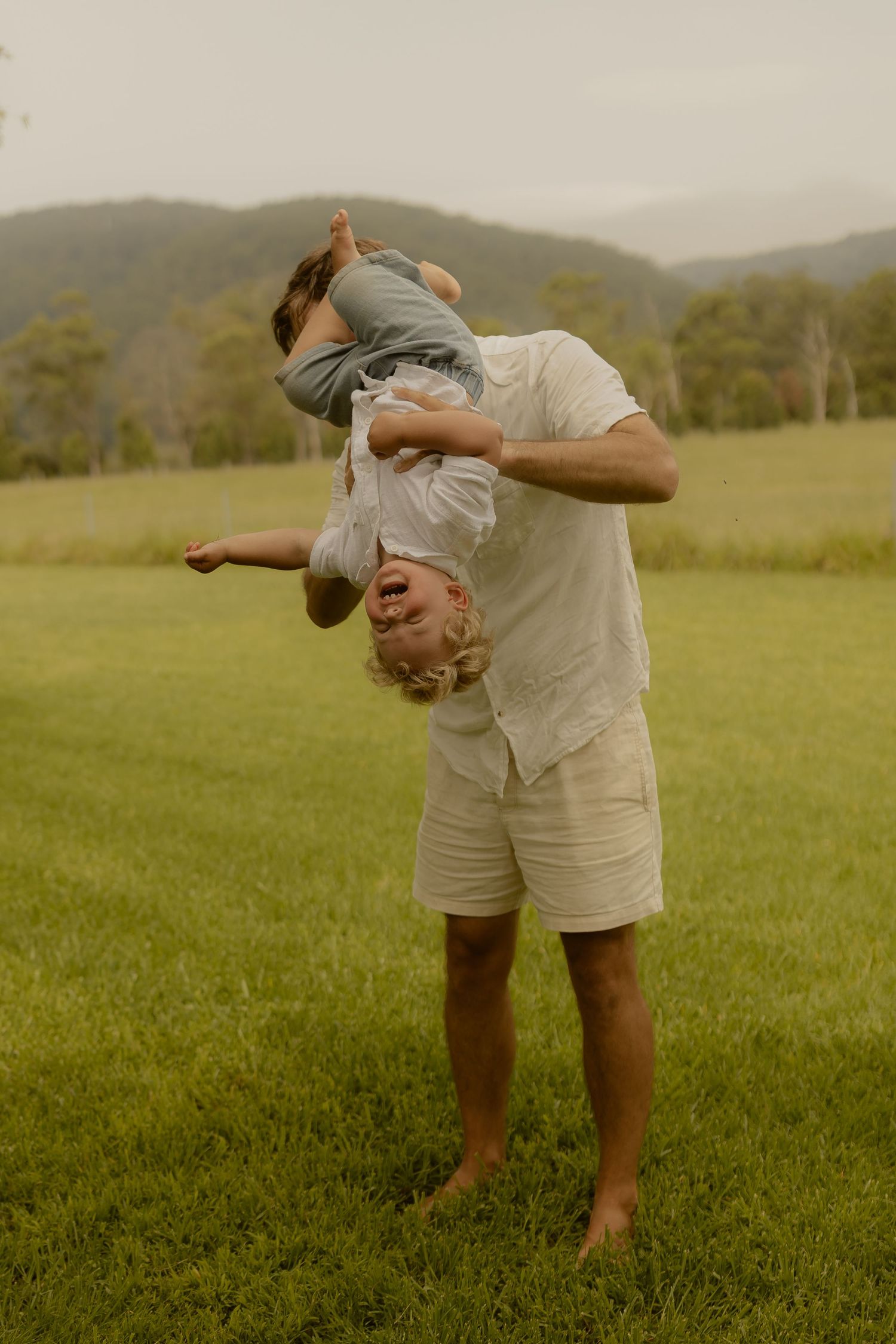 A playful moment captured in a green field with mountains in the background shows joyful outdoor fun.