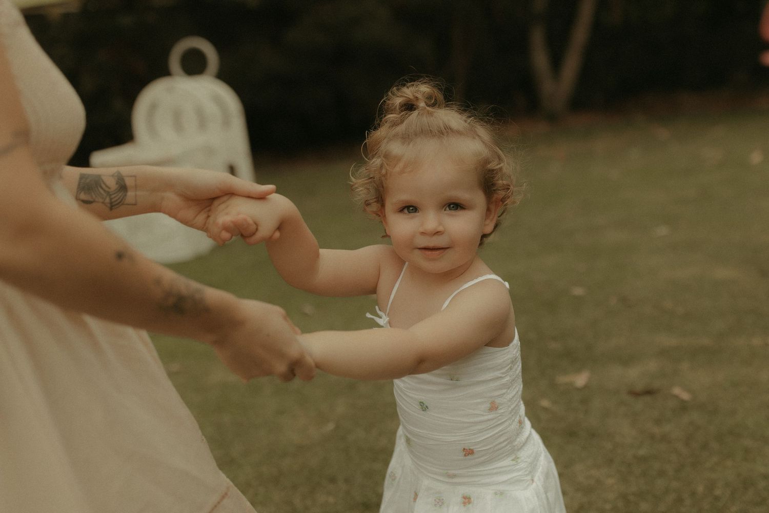 A small child in a white dress dances and holds hands in a garden setting.