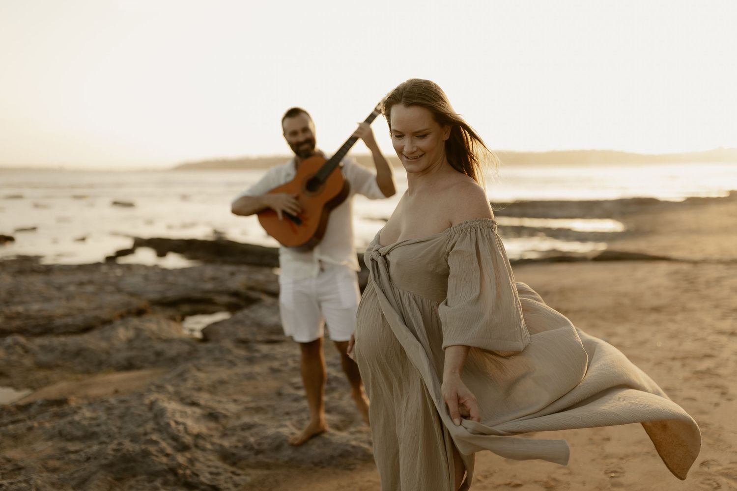 Couple enjoying a carefree moment together on a sandy beach at dusk with ocean waves crashing nearby.