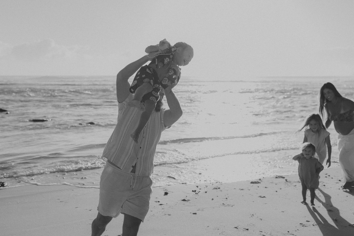 Black and white beach photography session capturing natural family interactions at sunset.