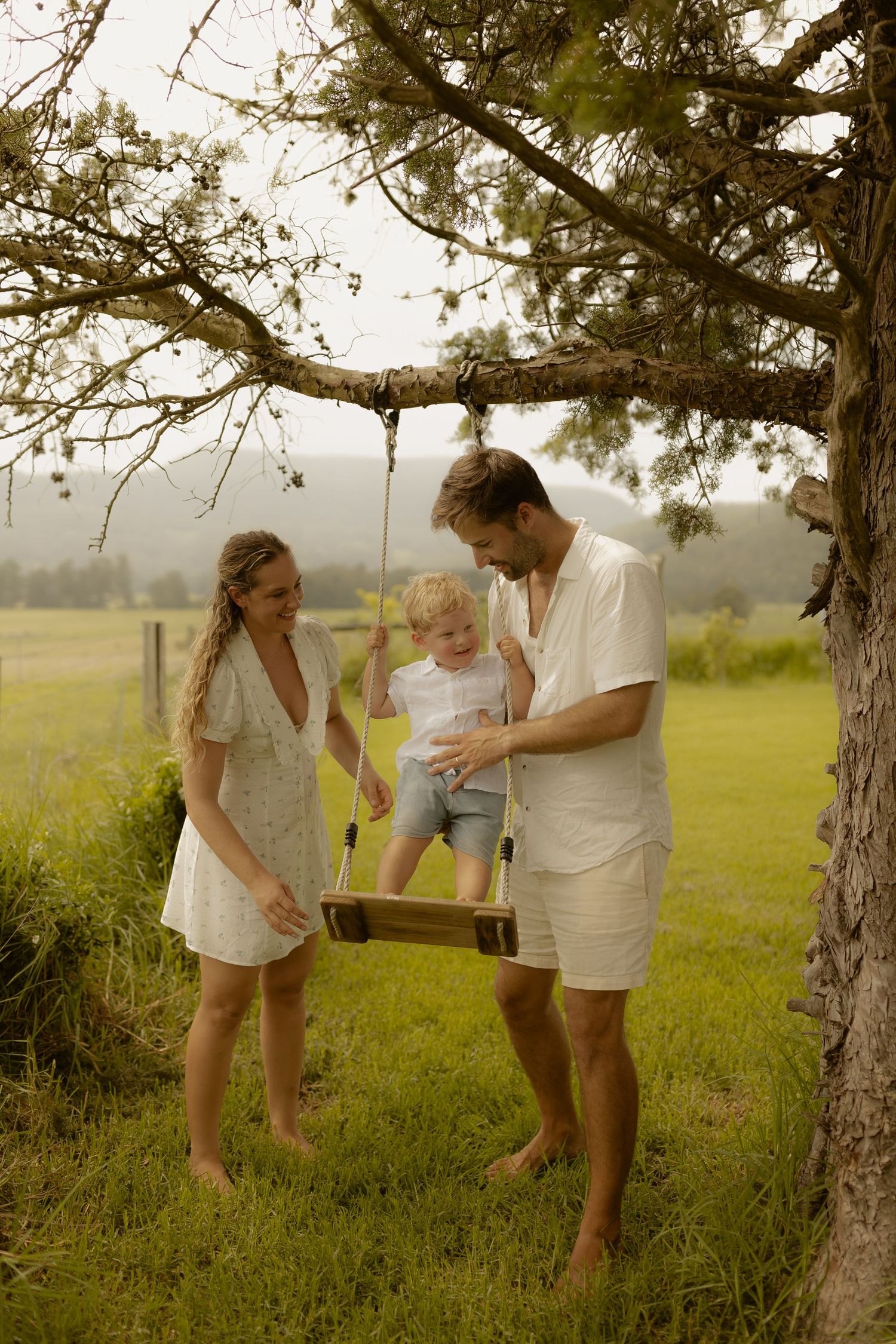 A playful family moment captured under a large tree in a sunny meadow.