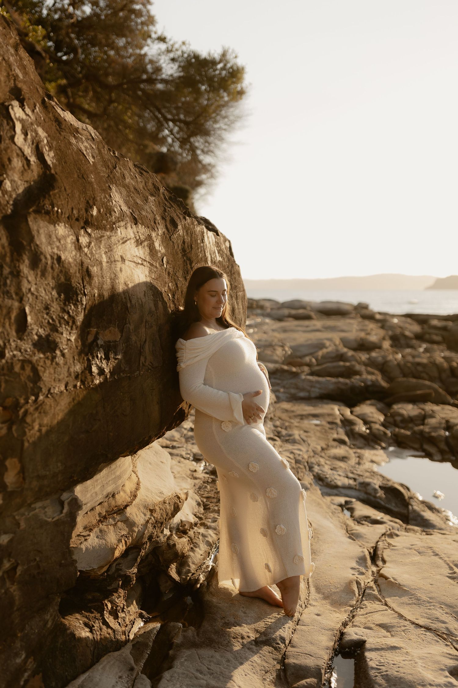 A person in white standing against rocky coastal cliffs during golden hour.