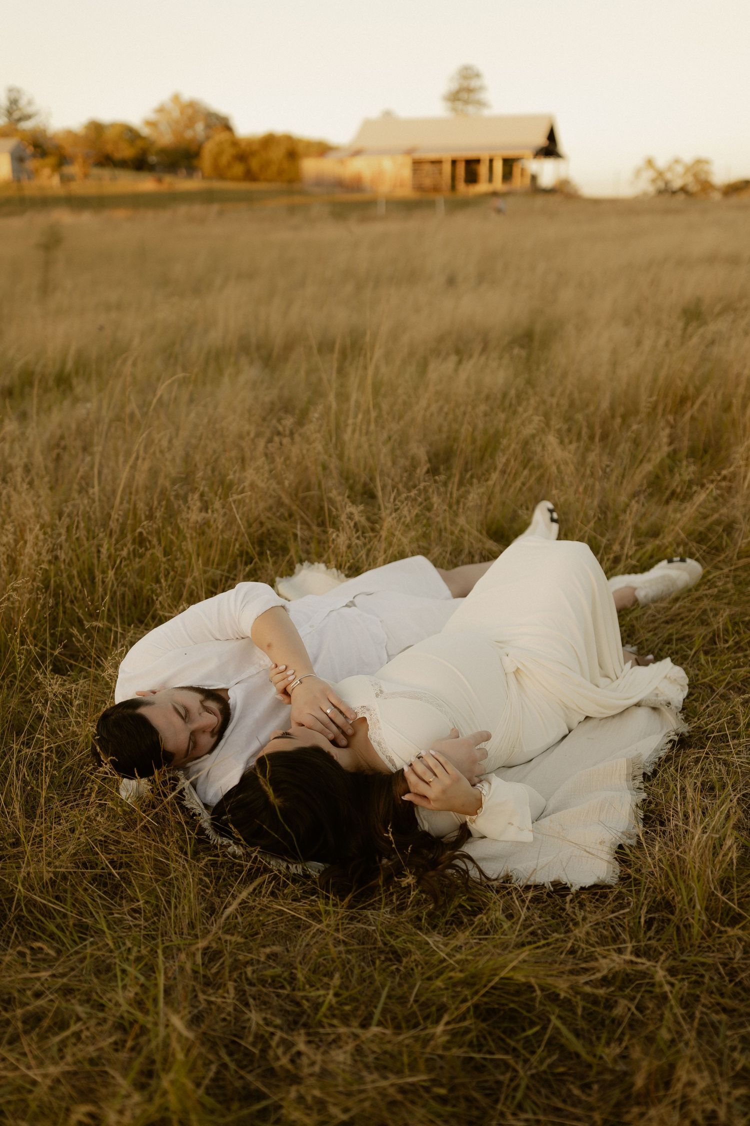 Figure in flowing white dress lying peacefully in golden grass field during sunset.