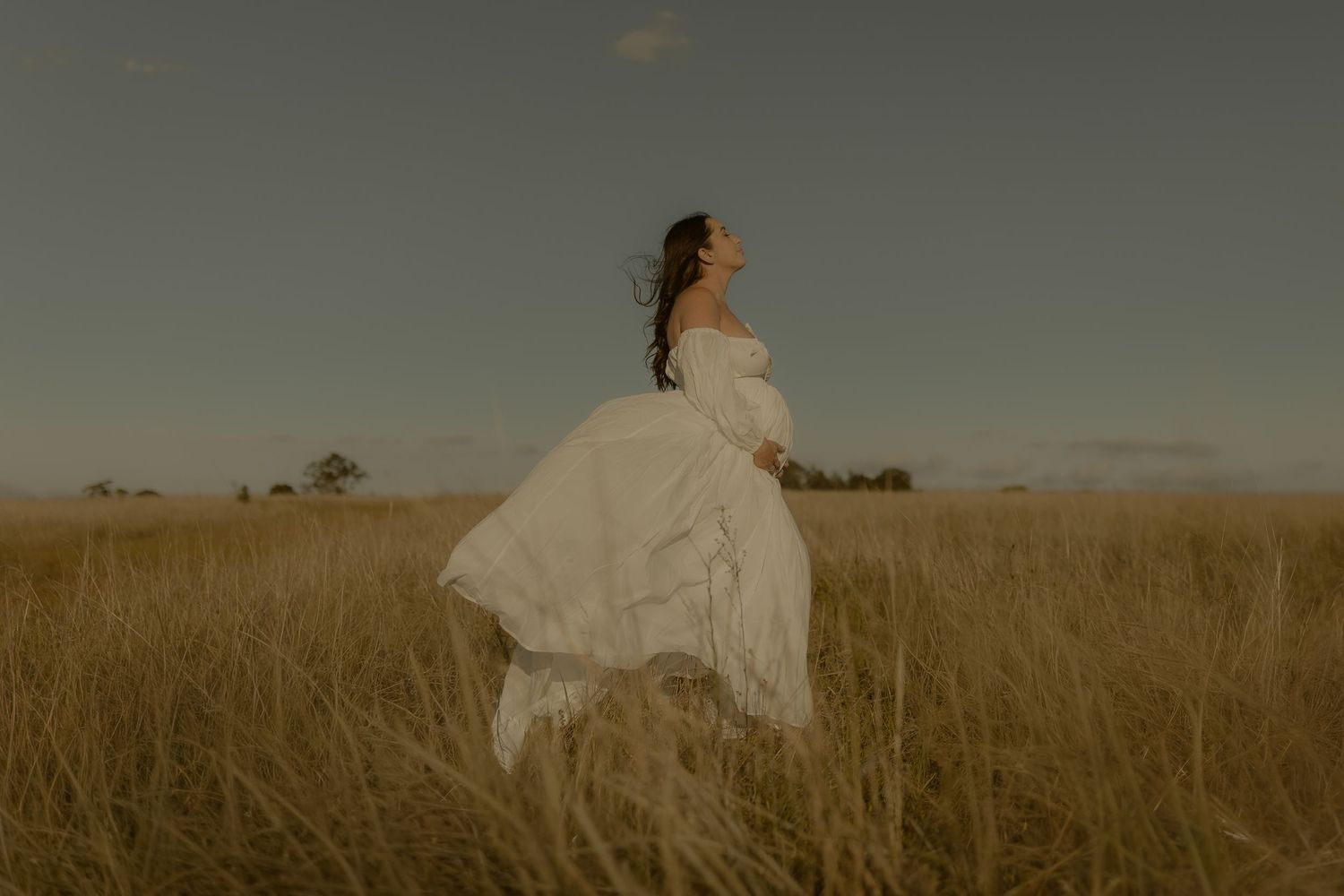 A person in a flowing white dress twirls gracefully in a golden wheat field at sunset.