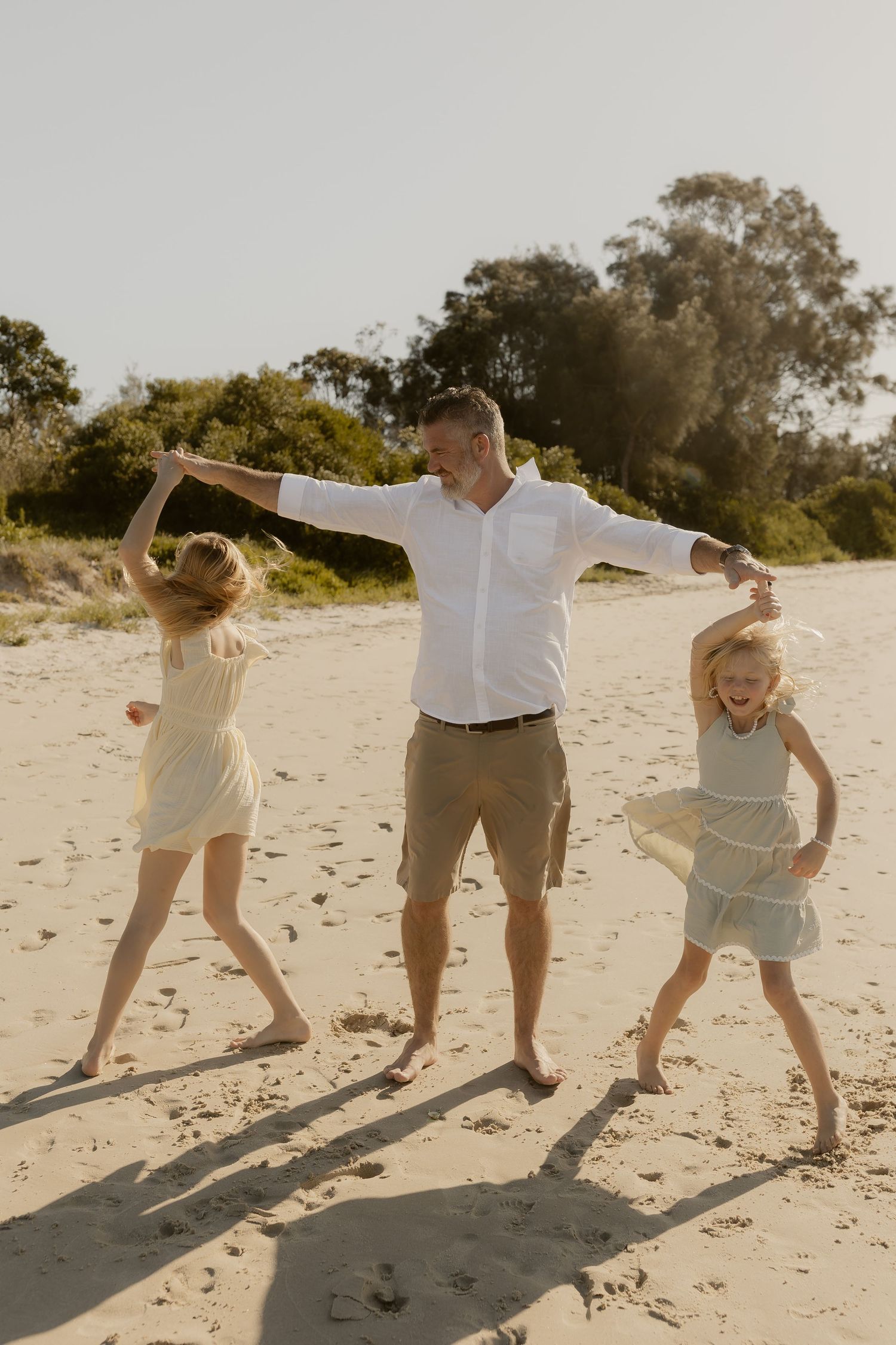 A playful sequence of people running and jumping on a sunny beach with long shadows cast on the sand.