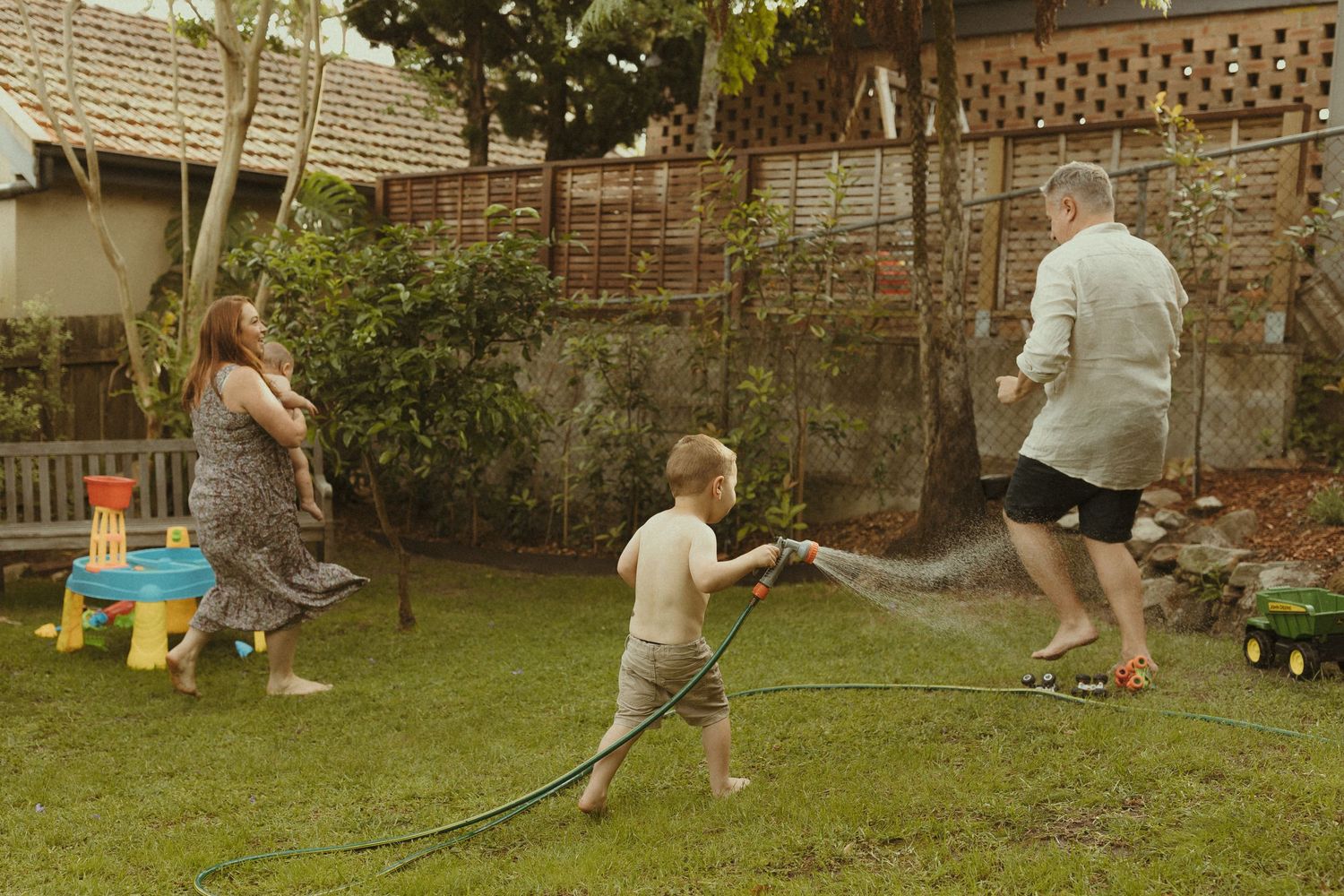 People playing and running through sprinklers in a backyard garden on a sunny day.