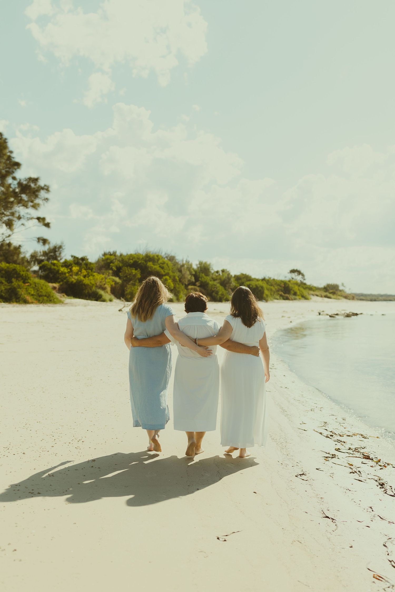 Three people walking arm in arm along a serene beach shoreline at sunset.