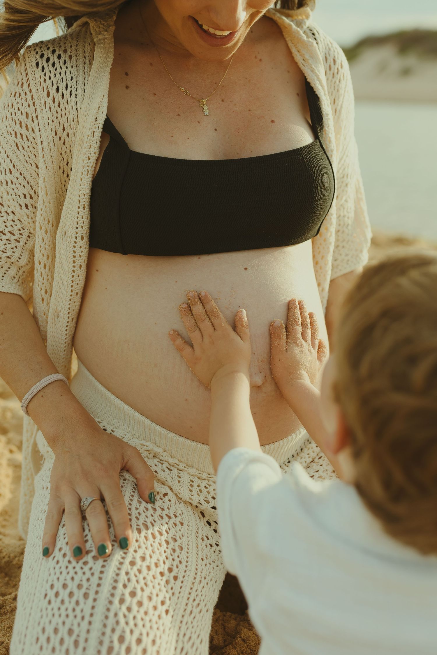 A tender maternity moment shows small hands touching a pregnant belly.