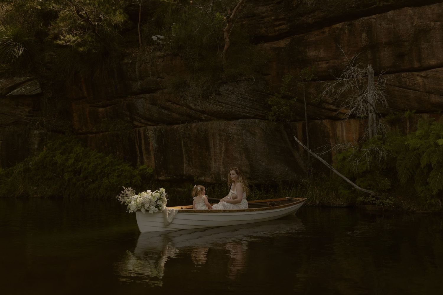 Scenic river view with small boats moored along a rocky cliff face in a tranquil natural setting.