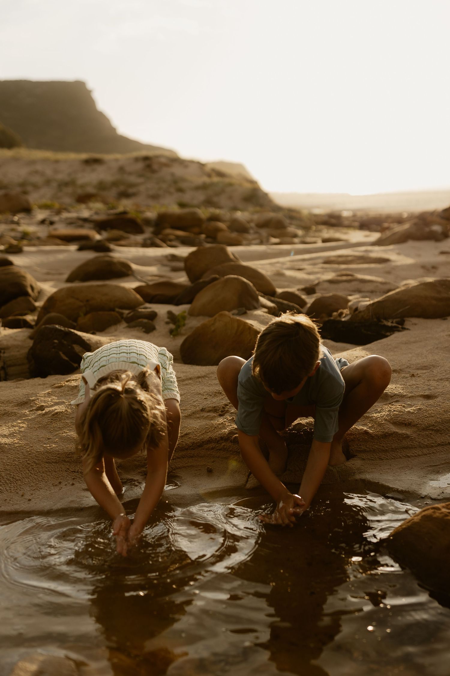 People exploring tidal pools among coastal rocks during golden hour.