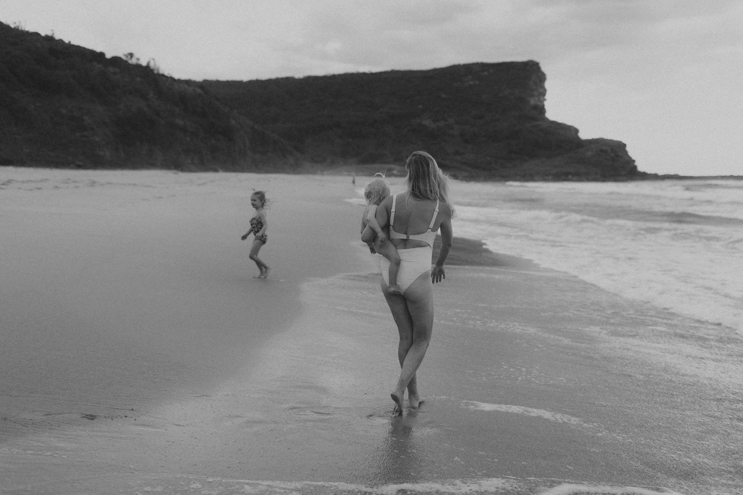 People walking along a scenic black and white beach with cliffs in the background.