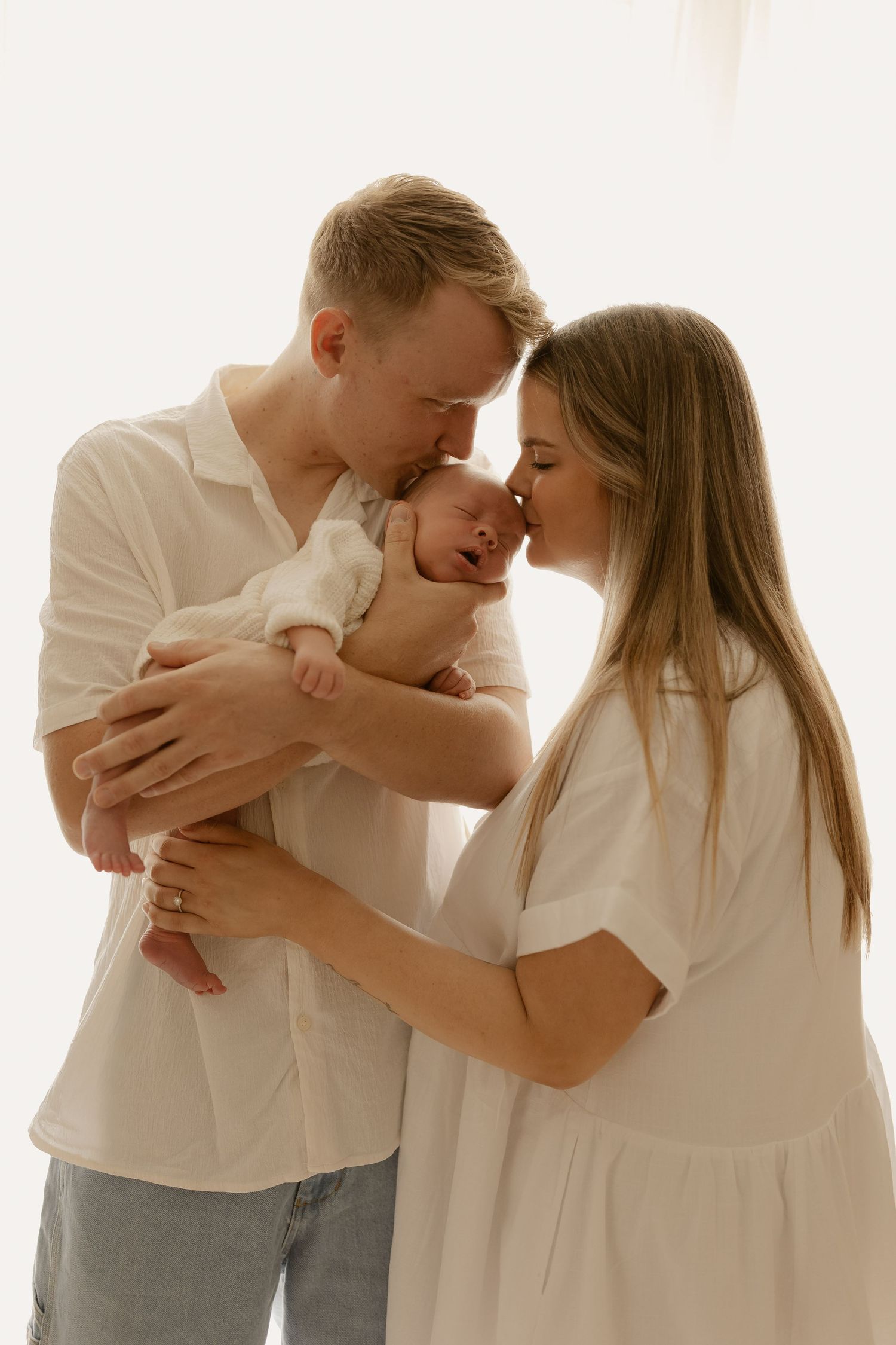 A couple in white outfits sharing tender moments with their baby in a minimalist photo series.