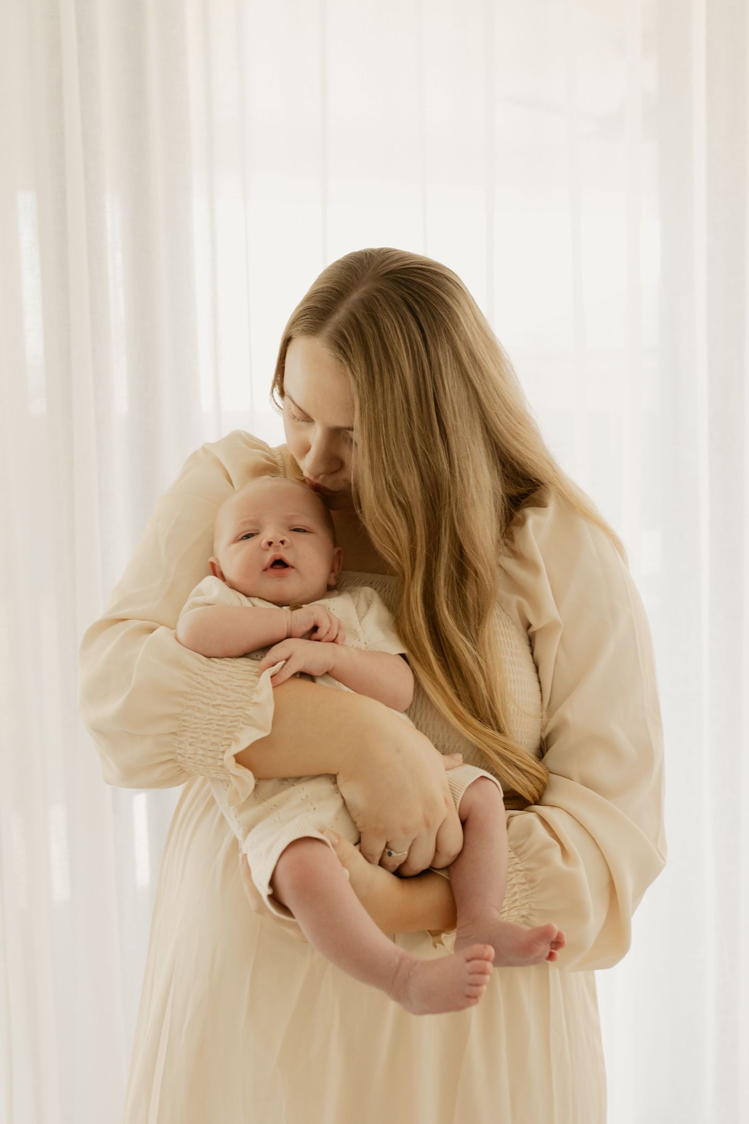 Tender moment captured as parent cradles sleeping infant against beige sweater by sunlit window.