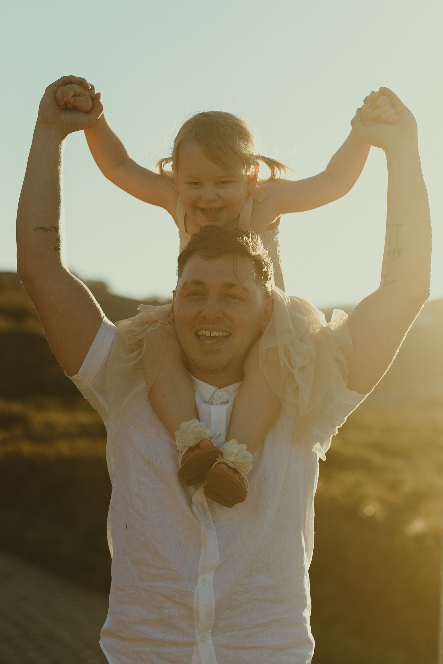 A tender moment captured in golden sunlight as a parent and child share joyful laughter during a shoulder ride outdoors.