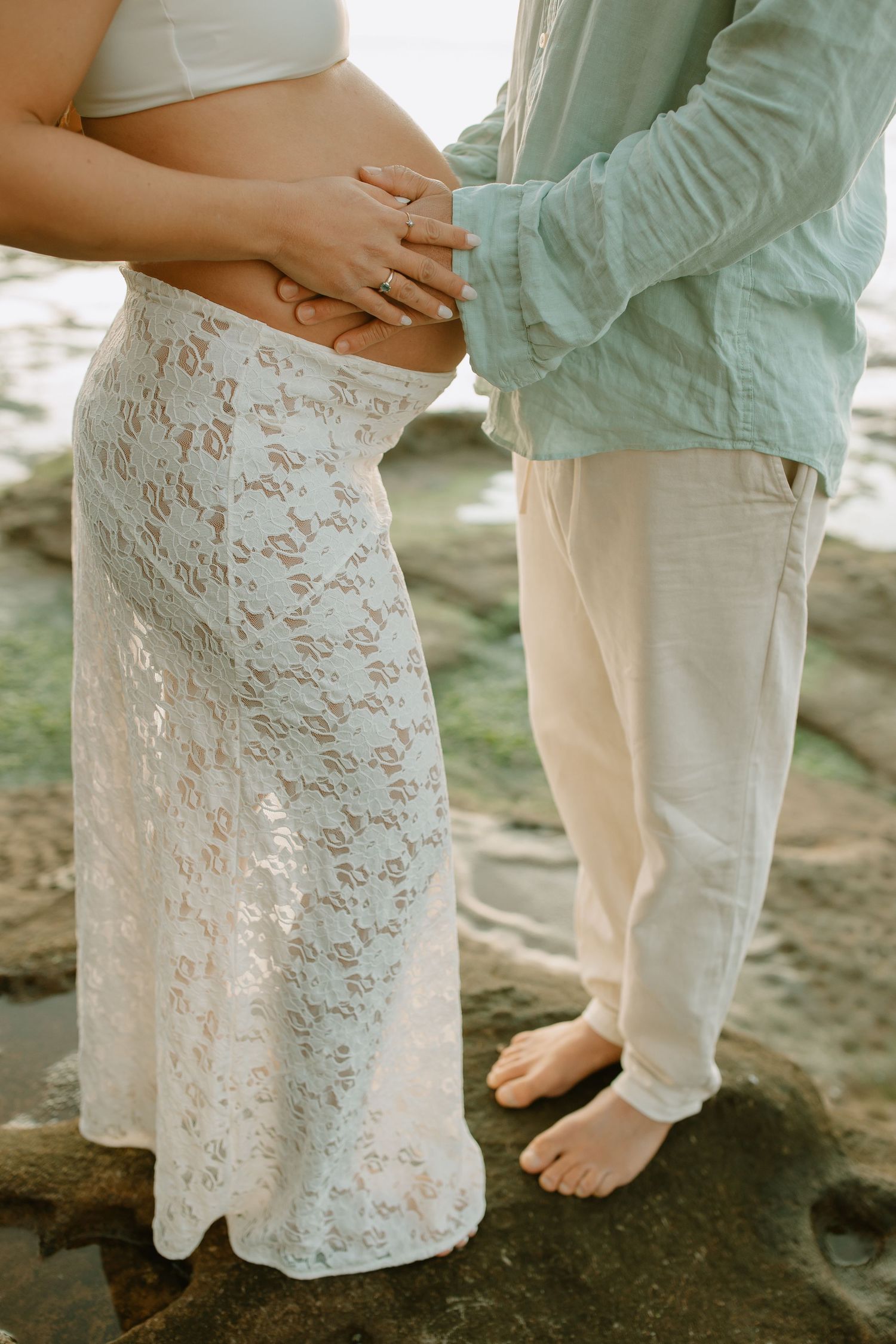 A couple shares an intimate moment on rocky terrain, wearing white and mint colored clothing.