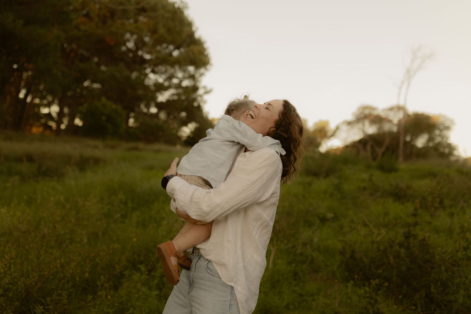 A couple embraces in a romantic moment at sunset in a grassy field during golden hour.