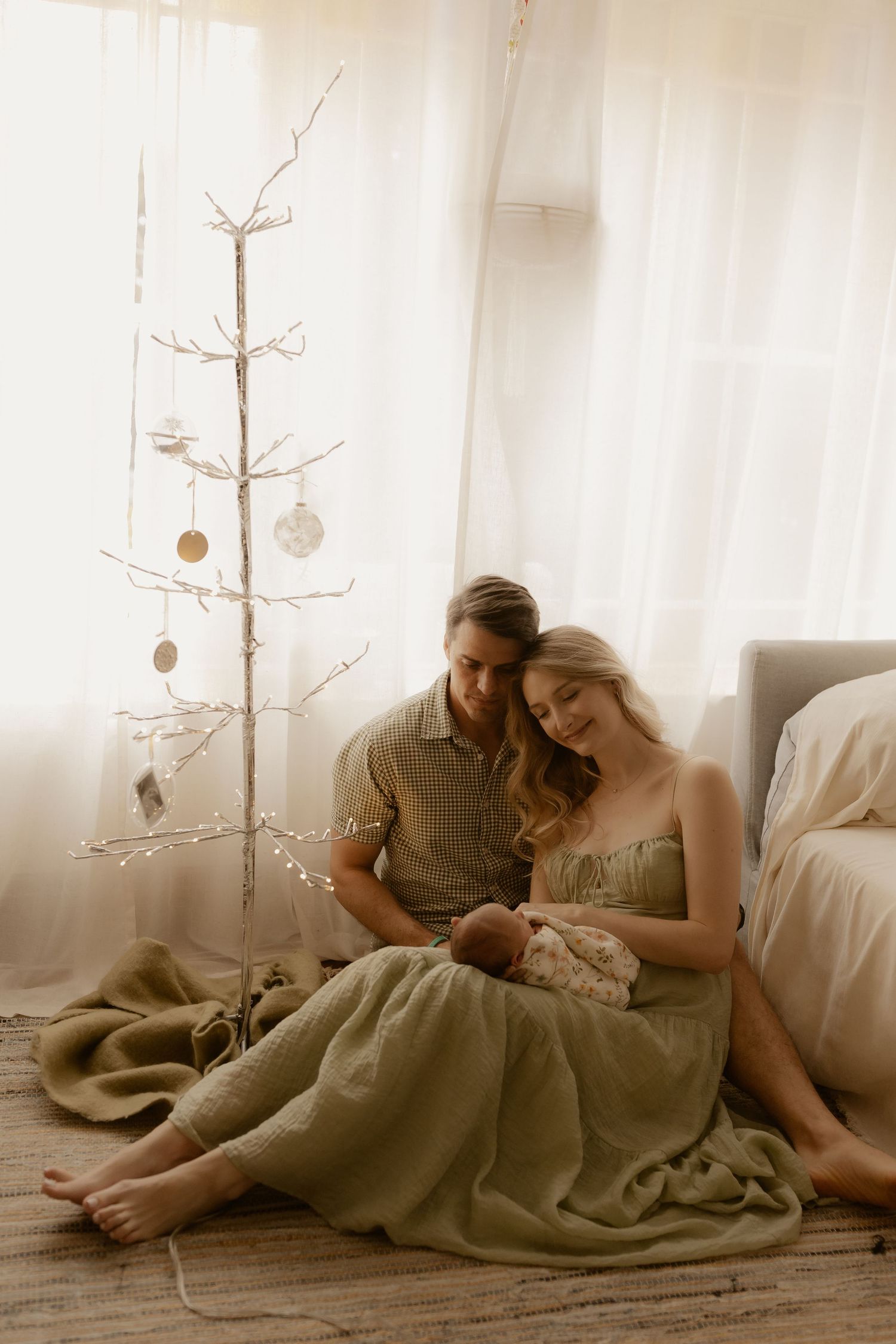 Family resting together on floor with minimalist white Christmas tree decoration in background.