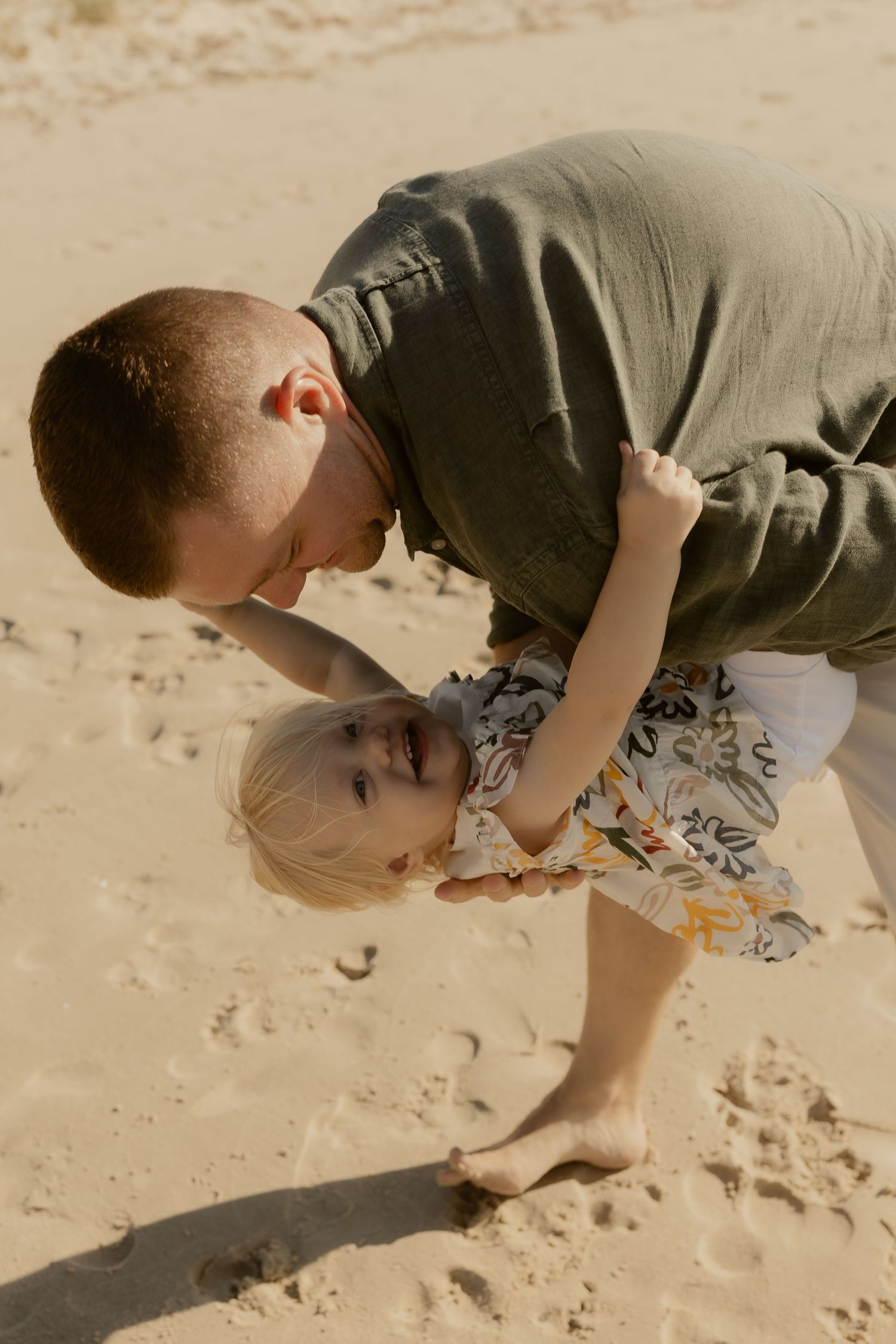 Parent and child playing in the sand during a beach photoshoot.