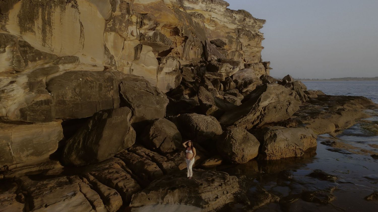 Rocky coastal cliffs with eroded sandstone formations along a rugged shoreline at sunset.