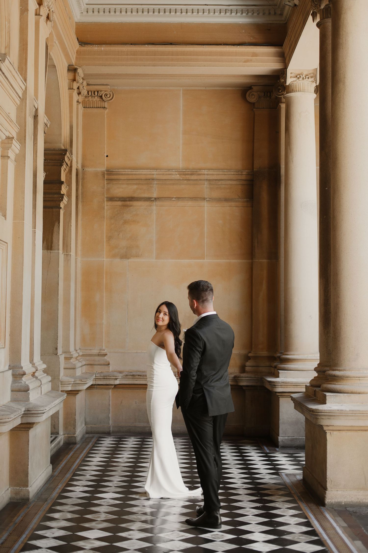 Elegant wedding portrait in historic hallway with checkered floor and classical columns.