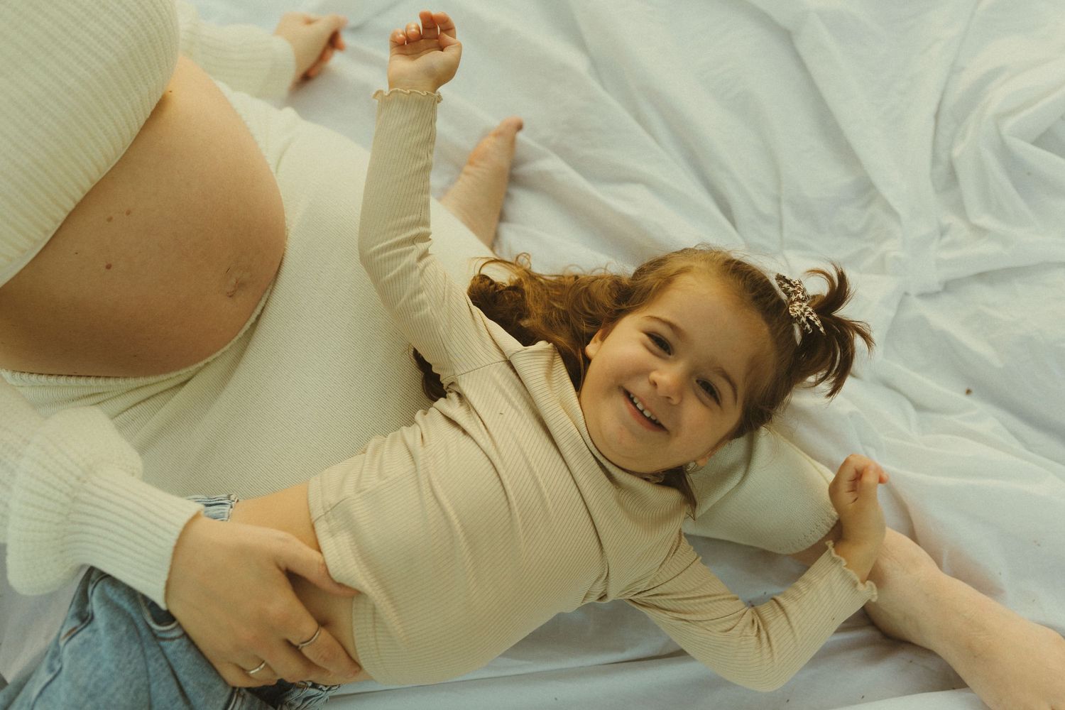 Child laying on white blanket outdoors with joyful expression and arms stretched wide.