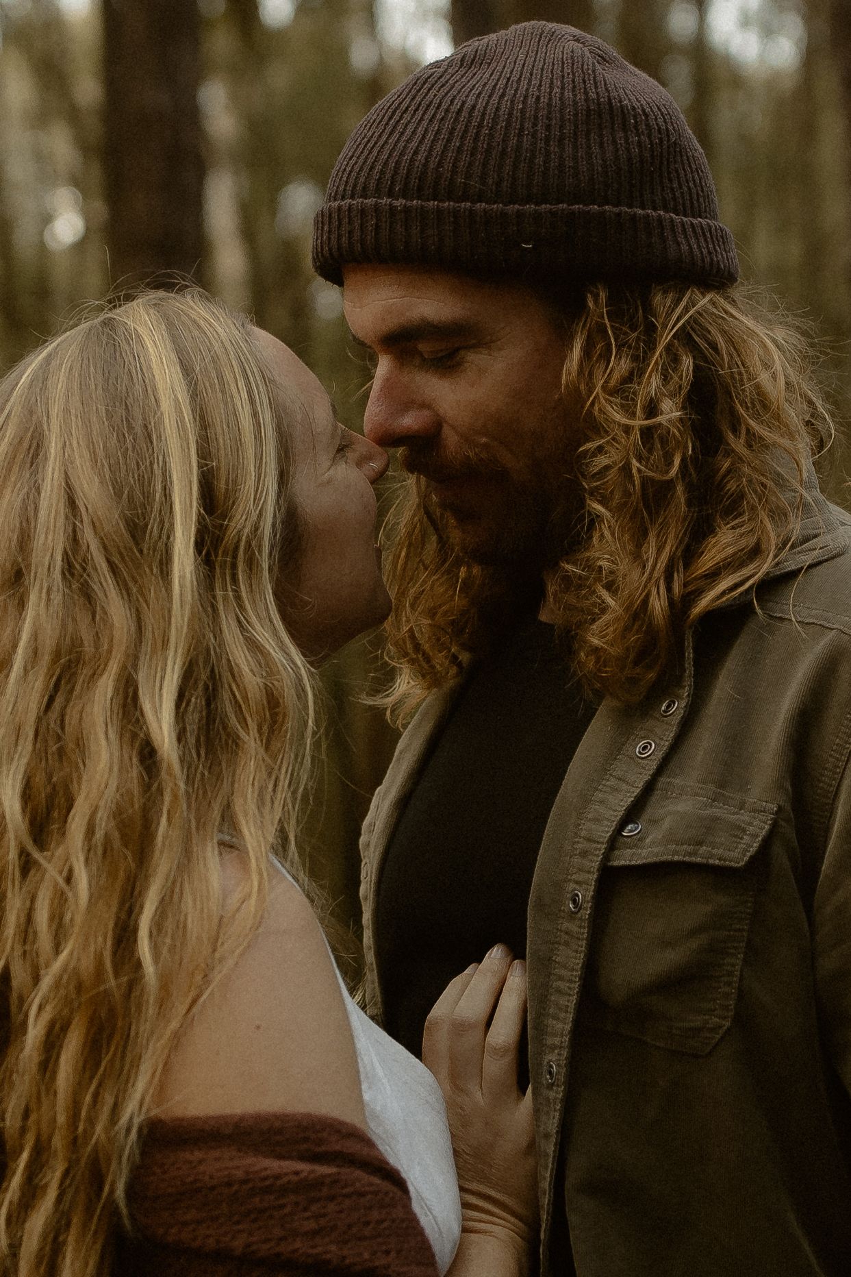 Romantic couple sharing an intimate moment in a forest setting with moody autumn colors and artistic lighting.