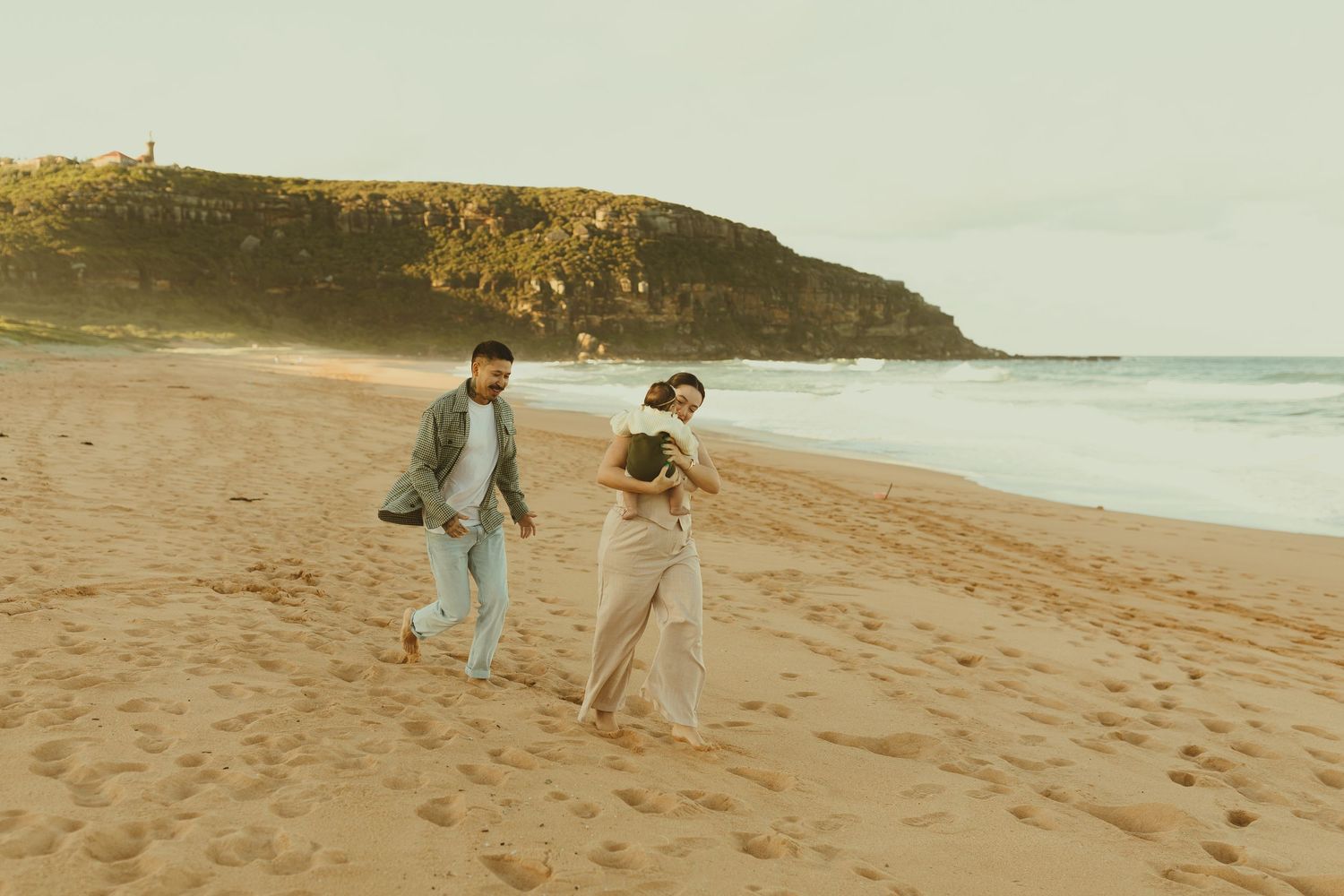 Coastal beach wedding at sunset with couple walking along sandy shore near cliffs and ocean.