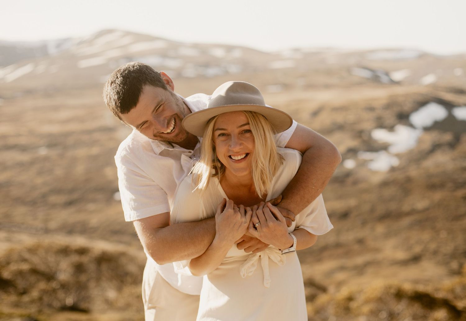 A couple shares an intimate moment together in casual attire against a scenic desert mountain backdrop at sunset.