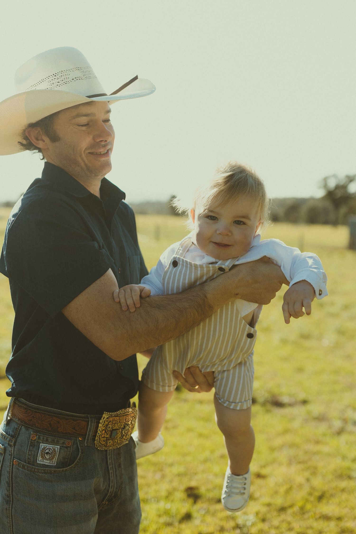 Playful outdoor moment in a sunny field wearing cowboy hats and western attire.