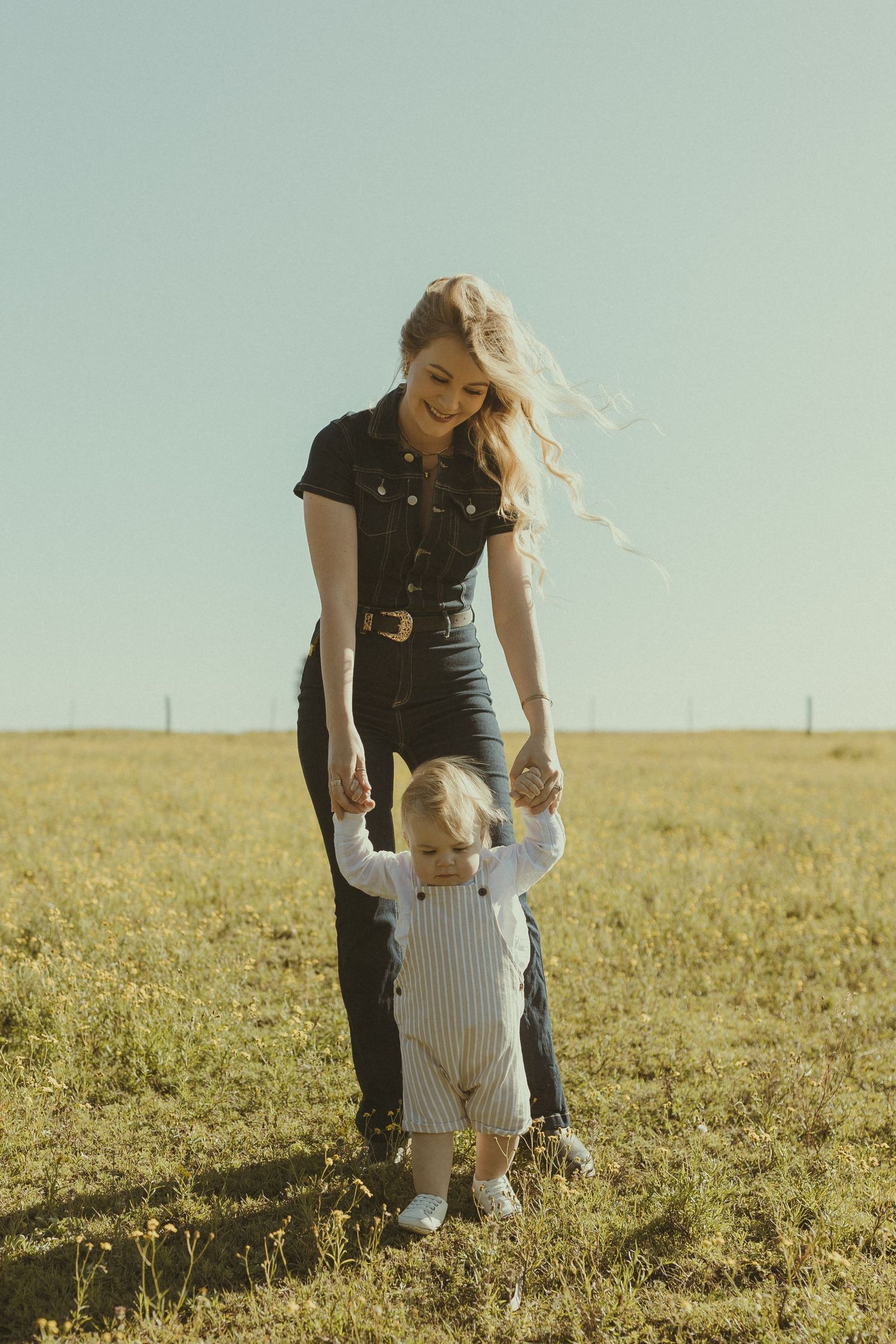 A parent and toddler walking together in a golden sunlit meadow.