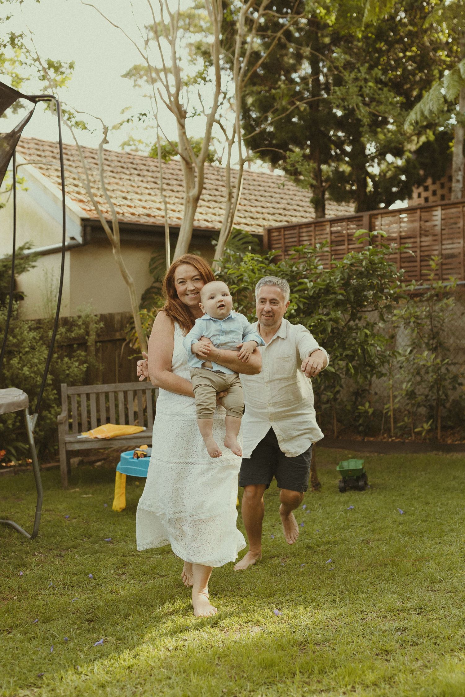 Family enjoying playful moments together in a backyard garden, swinging and laughing on a sunny day.